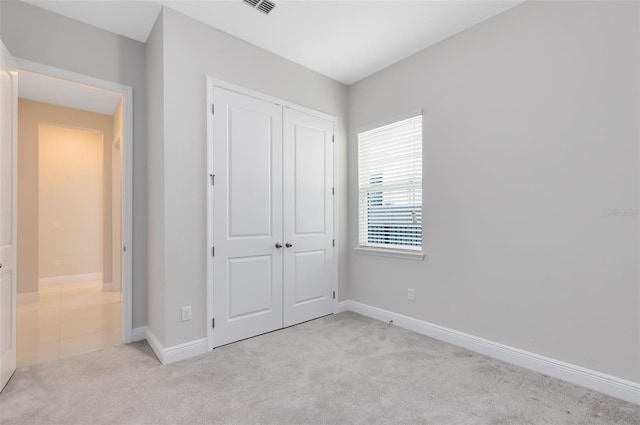 unfurnished bedroom featuring baseboards, a closet, visible vents, and light colored carpet