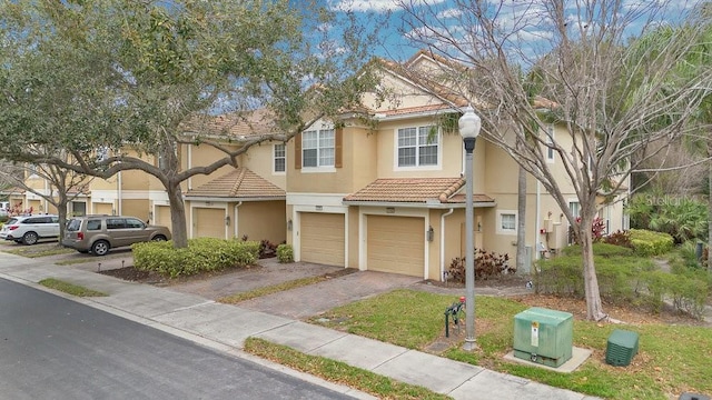 townhome / multi-family property featuring a tiled roof, aphalt driveway, an attached garage, and stucco siding