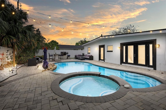 pool at dusk with french doors, a pool with connected hot tub, a patio area, fence, and an outdoor living space