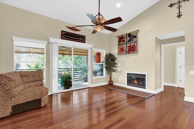 unfurnished living room featuring a glass covered fireplace, ceiling fan, wood finished floors, high vaulted ceiling, and baseboards