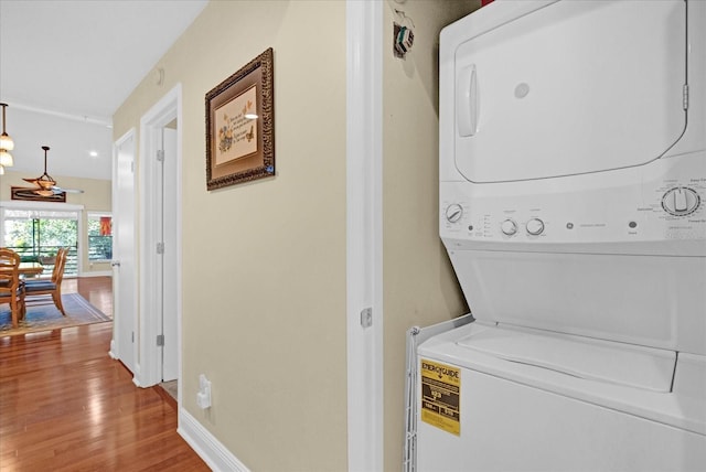 laundry area featuring stacked washer and dryer, laundry area, baseboards, and wood finished floors