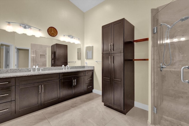 full bathroom with double vanity, a shower stall, baseboards, and a sink