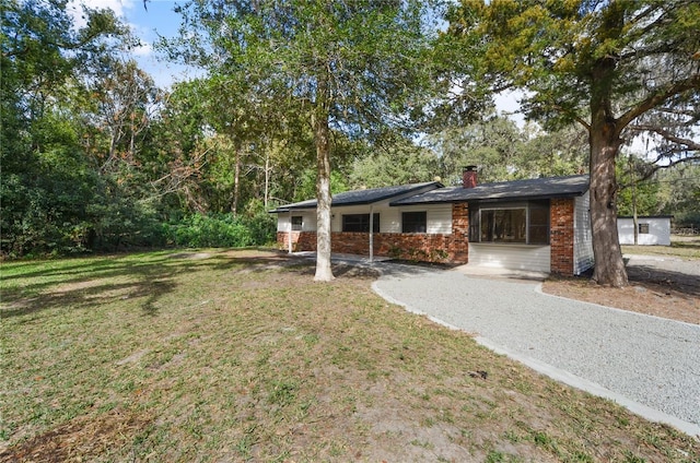 ranch-style home featuring driveway, brick siding, a chimney, and a front yard