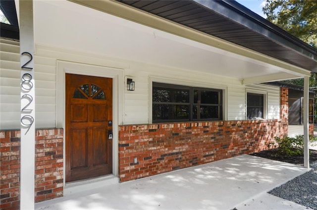 entrance to property featuring covered porch and brick siding