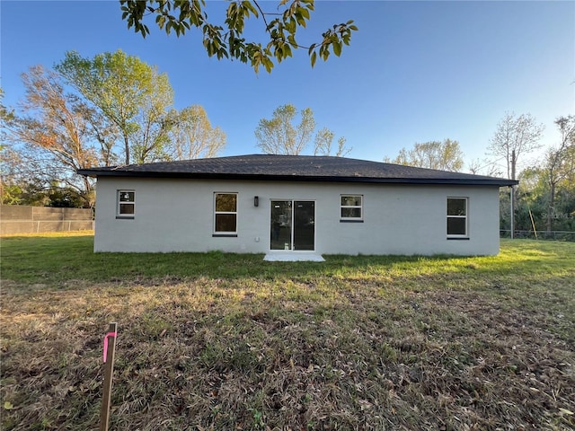 rear view of house featuring a yard, fence, and stucco siding