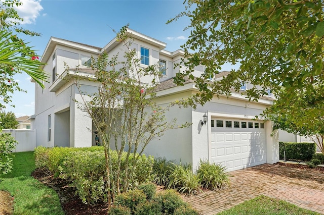 view of front facade with a garage, fence, decorative driveway, and stucco siding