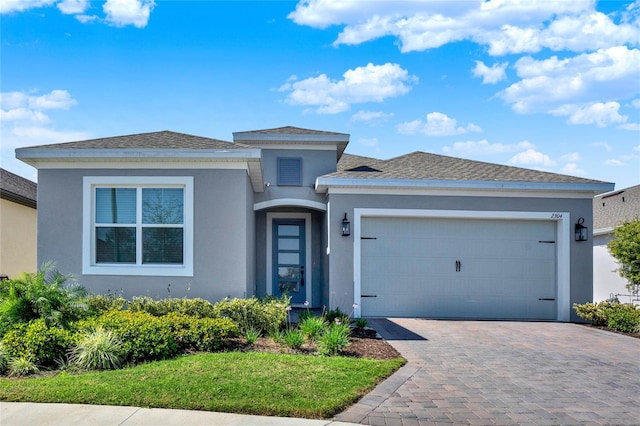 prairie-style home featuring an attached garage, decorative driveway, and stucco siding