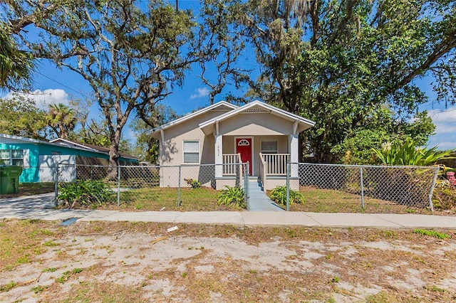 bungalow with covered porch, a fenced front yard, and stucco siding