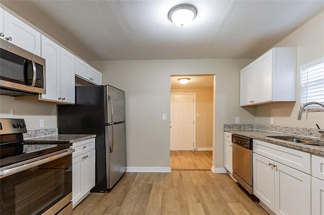 kitchen with light wood-style flooring, light stone countertops, stainless steel appliances, white cabinetry, and a sink