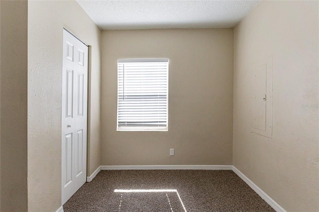 carpeted spare room with a textured ceiling, electric panel, and baseboards