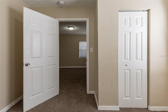 hall featuring dark carpet, a textured ceiling, and baseboards