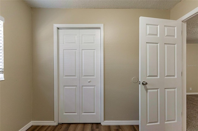 unfurnished bedroom featuring a textured ceiling, a closet, baseboards, and dark wood-type flooring