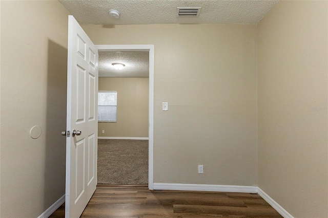 unfurnished room featuring visible vents, a textured ceiling, baseboards, and wood finished floors