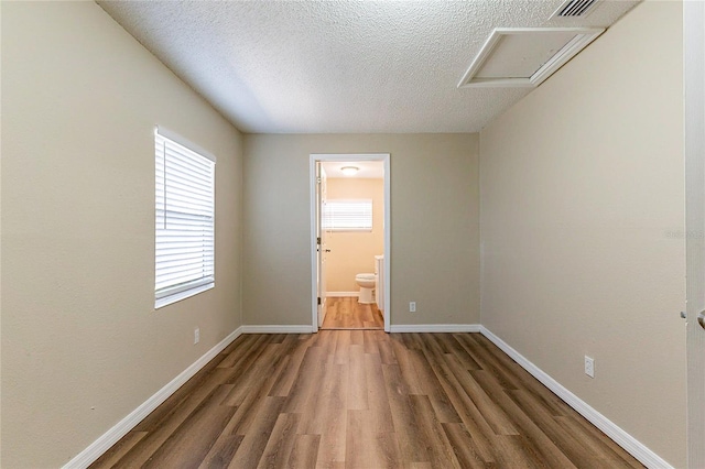 spare room with a textured ceiling, wood finished floors, visible vents, baseboards, and attic access