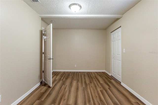 unfurnished room with a textured ceiling, baseboards, and wood finished floors