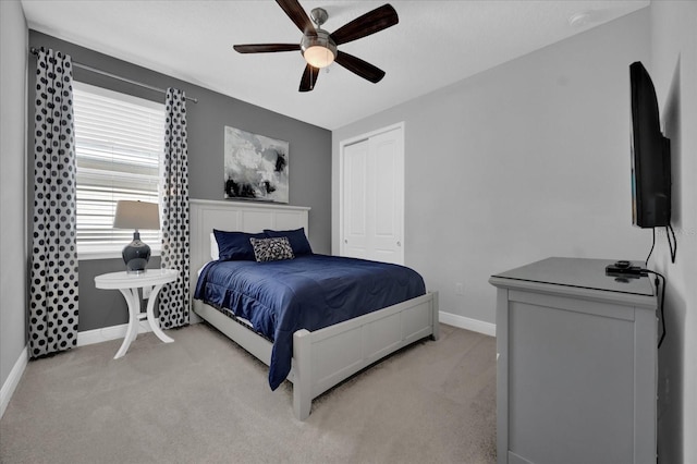 bedroom with baseboards, ceiling fan, a closet, and light colored carpet