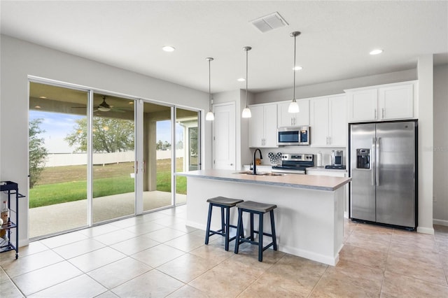 kitchen with a center island with sink, decorative light fixtures, stainless steel appliances, light countertops, and white cabinetry