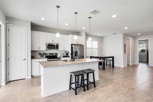 kitchen with light countertops, appliances with stainless steel finishes, a sink, and a center island with sink