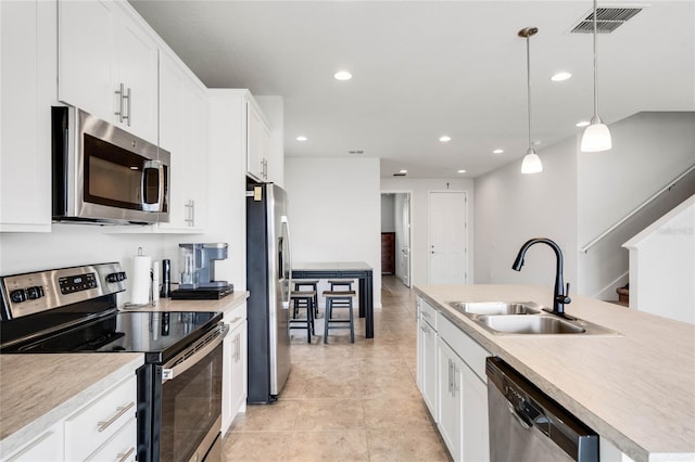 kitchen with white cabinets, appliances with stainless steel finishes, hanging light fixtures, light countertops, and a sink