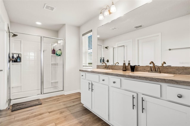 bathroom with visible vents, a sink, a shower stall, and wood finished floors