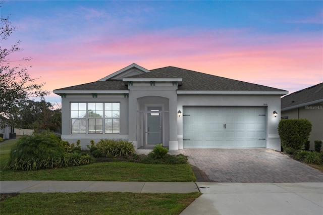 ranch-style home featuring an attached garage, roof with shingles, decorative driveway, and stucco siding