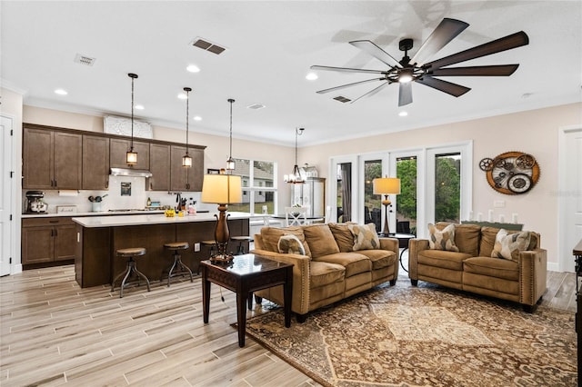 living room featuring a wealth of natural light, visible vents, crown molding, and light wood finished floors