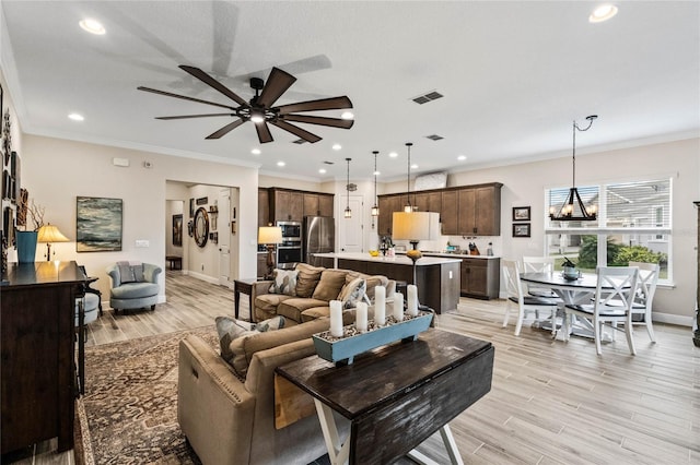 living room with ceiling fan with notable chandelier, light wood-type flooring, visible vents, and crown molding