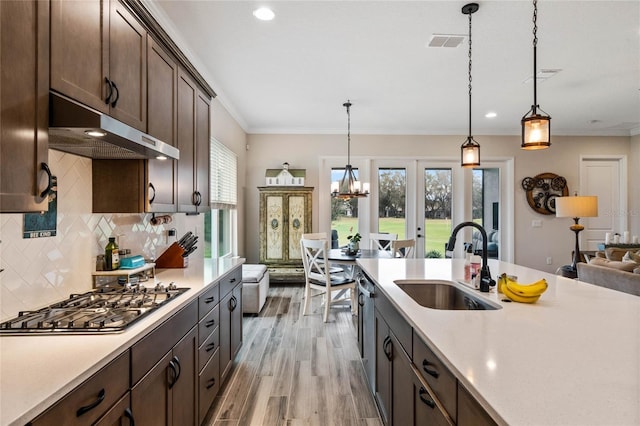 kitchen with decorative light fixtures, light countertops, stainless steel gas stovetop, a sink, and under cabinet range hood