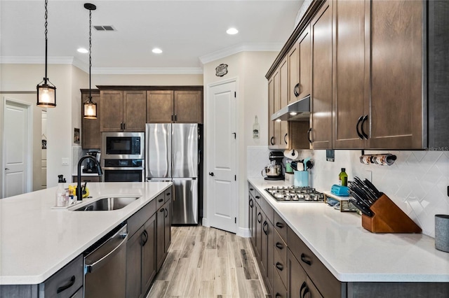 kitchen with appliances with stainless steel finishes, decorative light fixtures, light countertops, under cabinet range hood, and a sink