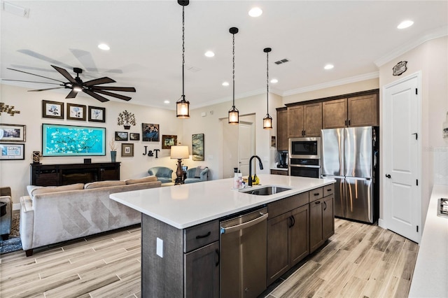 kitchen featuring appliances with stainless steel finishes, open floor plan, a kitchen island with sink, light countertops, and a sink