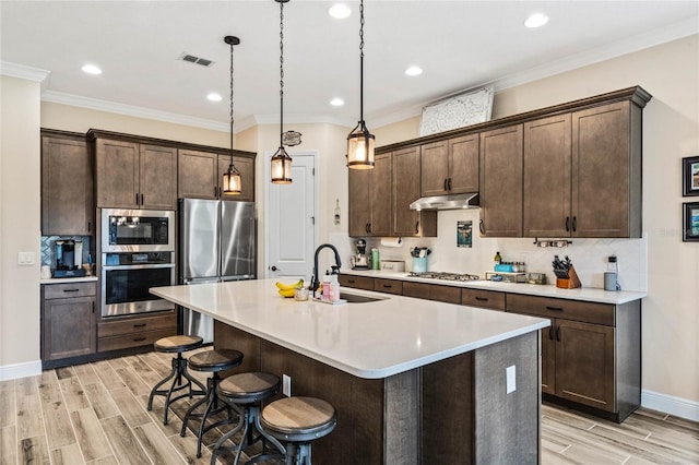 kitchen featuring stainless steel appliances, light countertops, under cabinet range hood, pendant lighting, and a sink