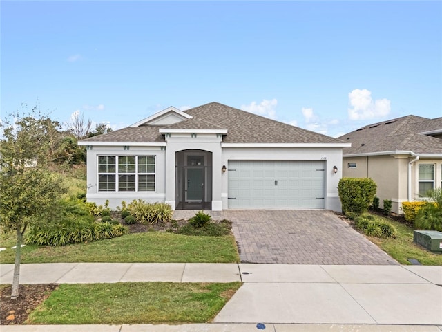 ranch-style house featuring an attached garage, a shingled roof, decorative driveway, stucco siding, and a front lawn