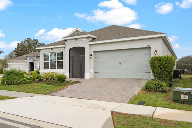 view of front of property featuring decorative driveway, stucco siding, a shingled roof, an attached garage, and cooling unit