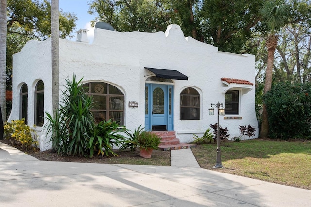 mediterranean / spanish house featuring a tiled roof, a front lawn, and stucco siding