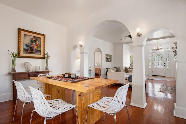 interior space featuring decorative columns, arched walkways, open floor plan, dark wood-style flooring, and ceiling fan with notable chandelier