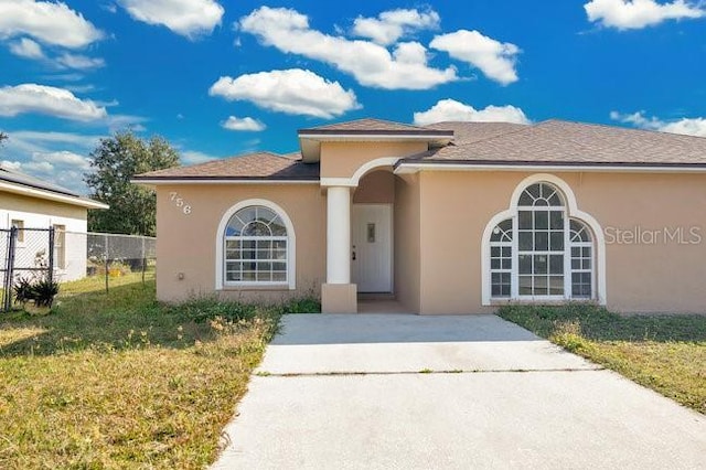 view of front of property with fence, a front lawn, stucco siding, and driveway