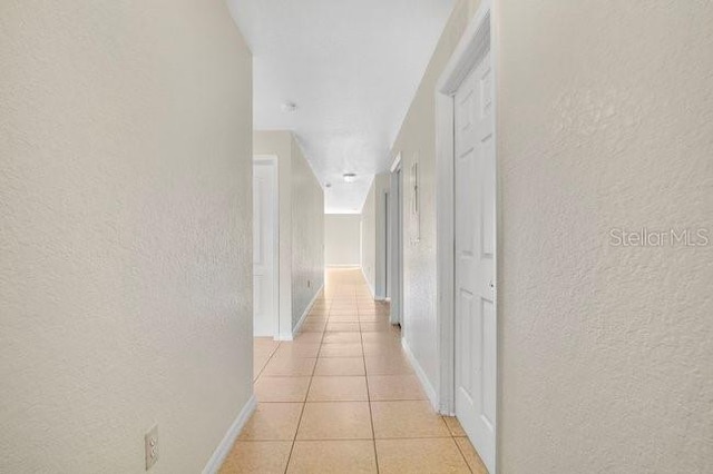 hallway with baseboards, light tile patterned floors, and a textured wall