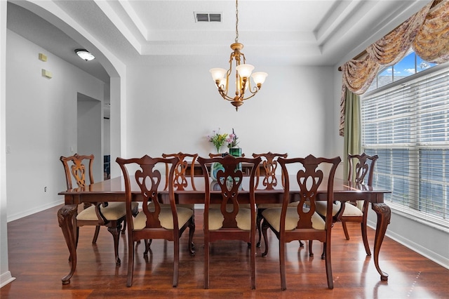 dining room with a raised ceiling, wood finished floors, visible vents, and a chandelier