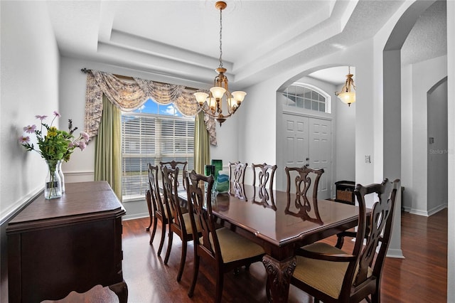 dining area featuring a tray ceiling, dark wood finished floors, arched walkways, baseboards, and a chandelier