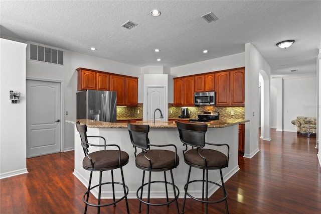 kitchen with stainless steel appliances, light stone countertops, visible vents, and an island with sink