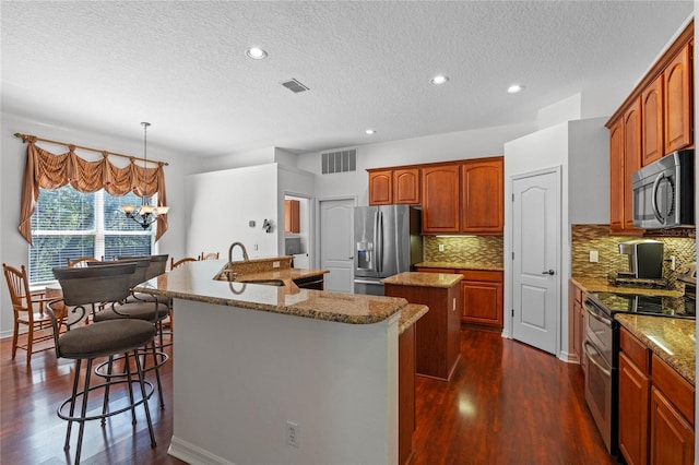 kitchen featuring visible vents, dark wood-type flooring, appliances with stainless steel finishes, and a kitchen island with sink