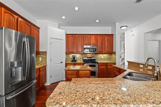 kitchen featuring dark wood-type flooring, a center island with sink, a sink, tasteful backsplash, and stainless steel appliances