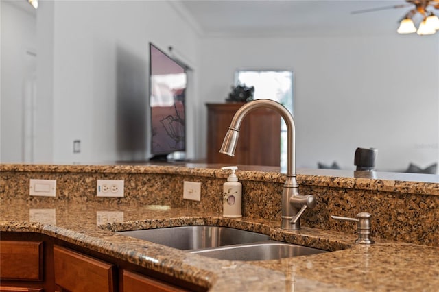 interior details featuring brown cabinets, a ceiling fan, a sink, stone countertops, and crown molding