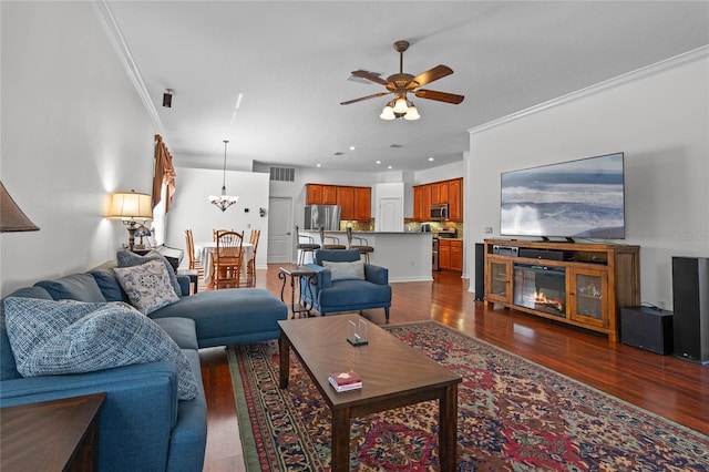 living room with ceiling fan with notable chandelier, a glass covered fireplace, dark wood finished floors, recessed lighting, and crown molding