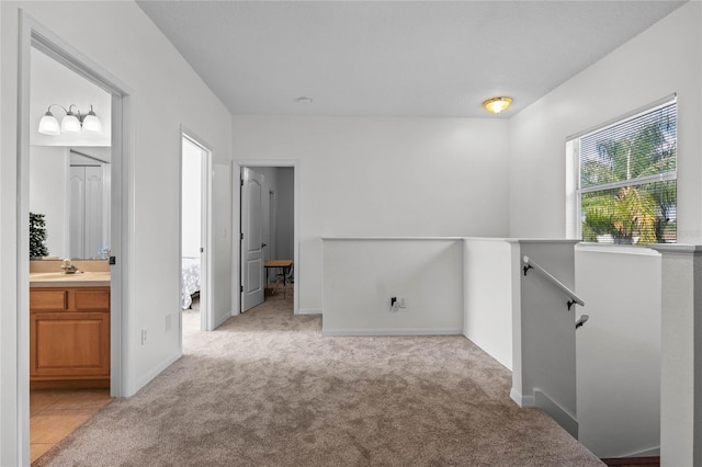 corridor featuring an upstairs landing, light colored carpet, baseboards, and a sink