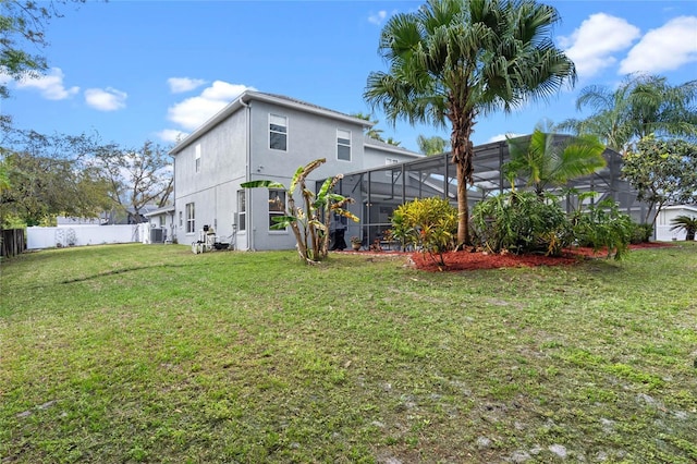 rear view of property featuring glass enclosure, fence, a lawn, and stucco siding