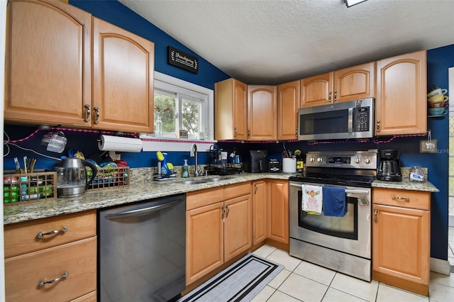 kitchen with appliances with stainless steel finishes, light tile patterned flooring, a sink, and light stone countertops