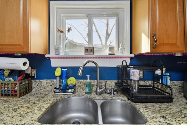 kitchen with brown cabinetry, a sink, and light stone counters