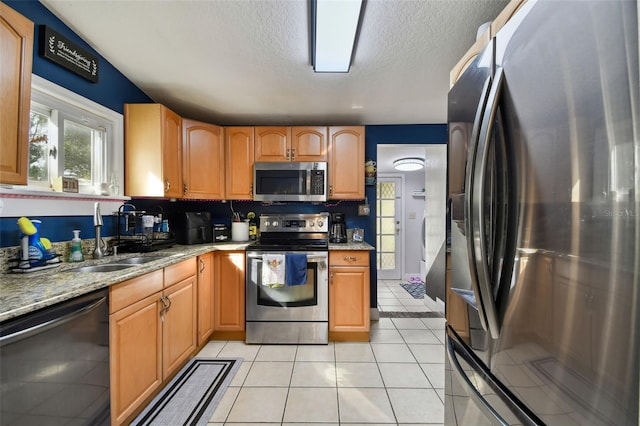 kitchen with light stone countertops, stainless steel appliances, a textured ceiling, a sink, and light tile patterned flooring