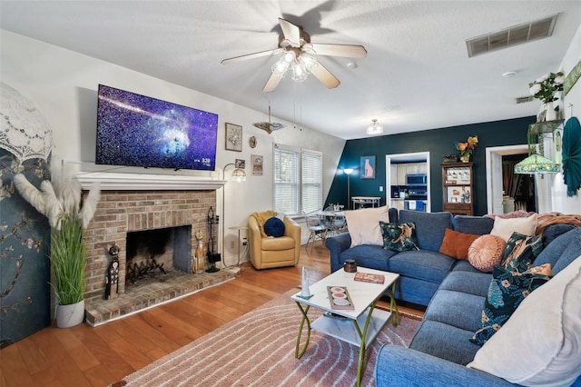 living area featuring ceiling fan, a brick fireplace, wood finished floors, and visible vents